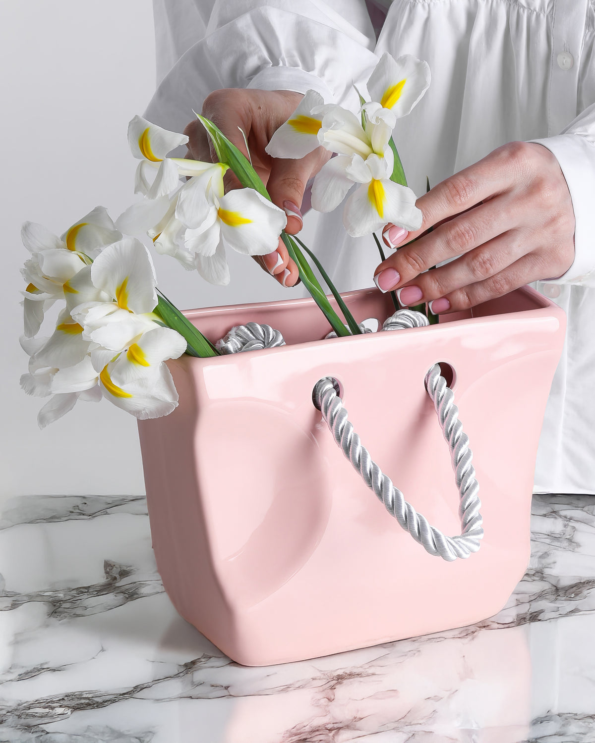 Blush pink ceramic purse vase with twisted rope handles on a soft surface, vanity home decor