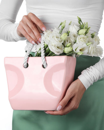 Blush pink ceramic handbag vase with rope handles filled with white flowers, coquette home decor