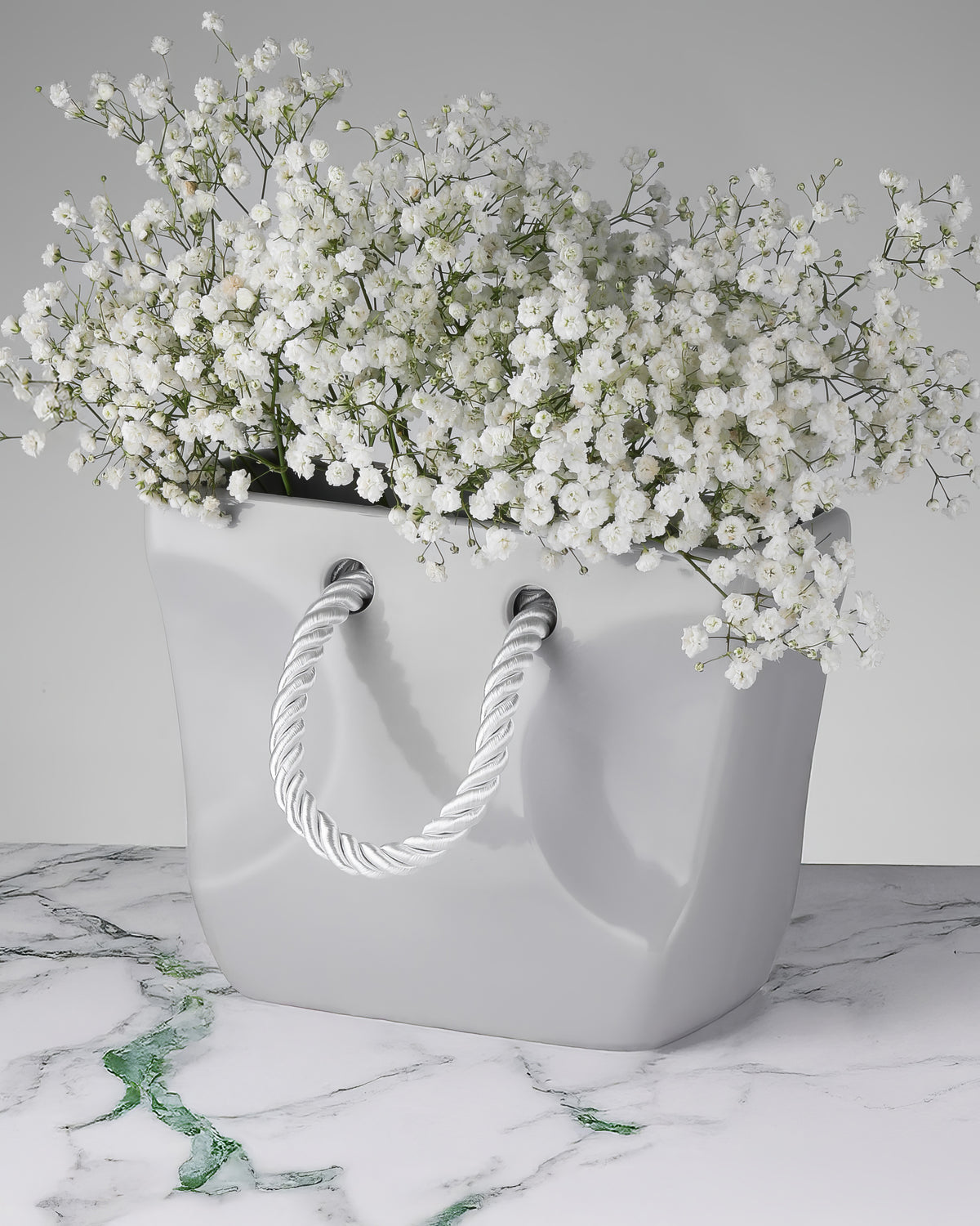 Stone-grey ceramic purse vase with twisted rope handles on a neutral surface, industrial home decor