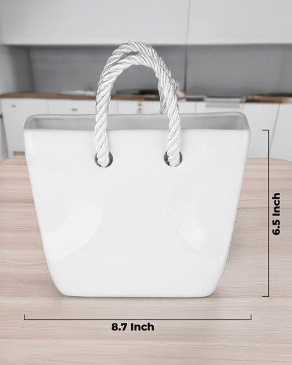 White ceramic purse vase with twisted rope handles held in hand against a plaid shirt, aesthetic flower vase